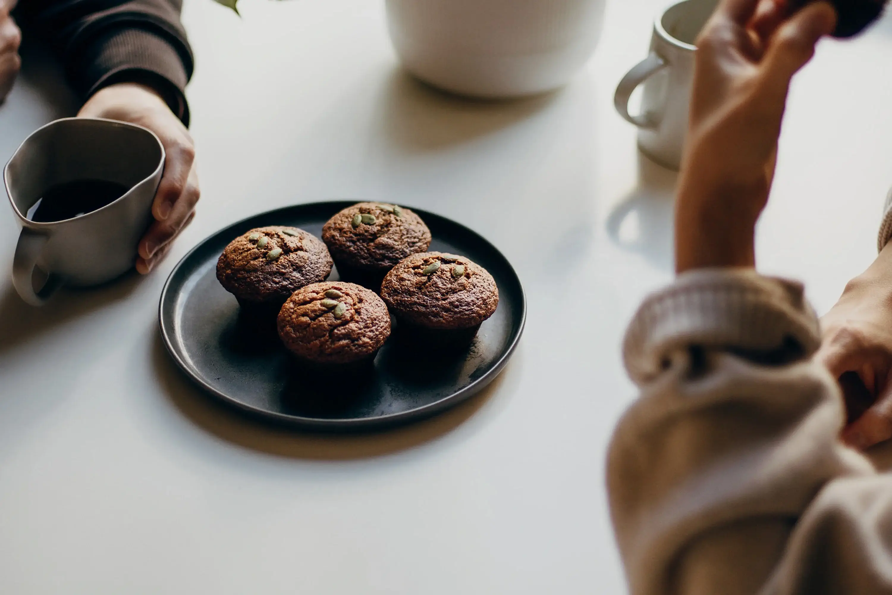 plate of 4 muffins with two sets of hands holding cups of tea